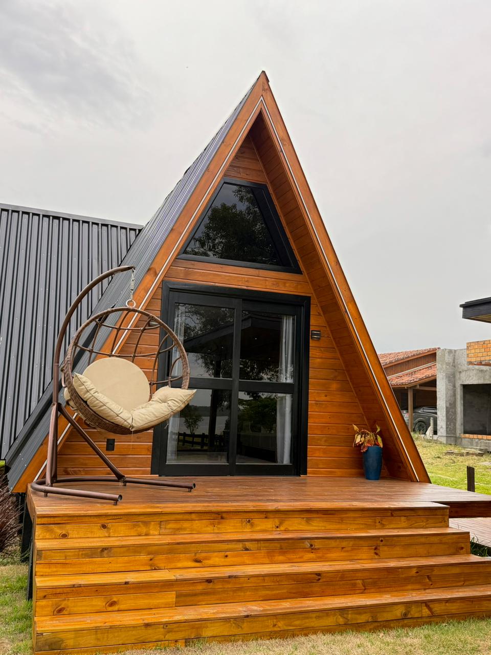 Chalé A-frame com varanda em madeira e cadeira suspensa